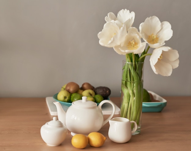 Hermoso servicio de té en mesa de madera. Decoración interior del hogar, ramo de flores en florero, mesa con juego de tetera.