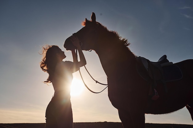 Hermoso sol Mujer joven de pie con su caballo en el campo de la agricultura durante el día