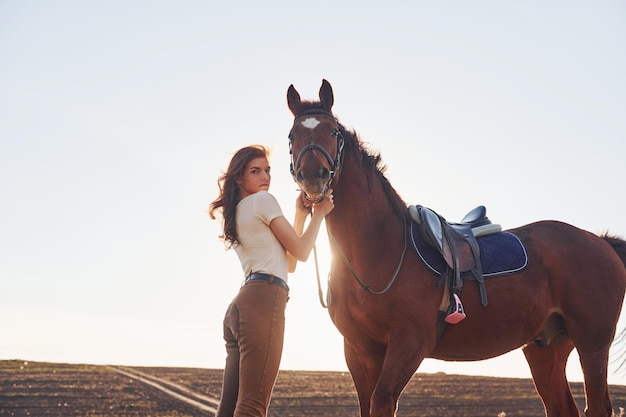 Hermoso sol Mujer joven de pie con su caballo en el campo de la agricultura durante el día