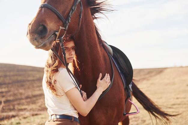 Hermoso sol Mujer joven de pie con su caballo en el campo de la agricultura durante el día