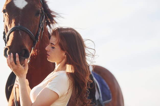 Foto hermoso sol mujer joven de pie con su caballo en el campo de la agricultura durante el día