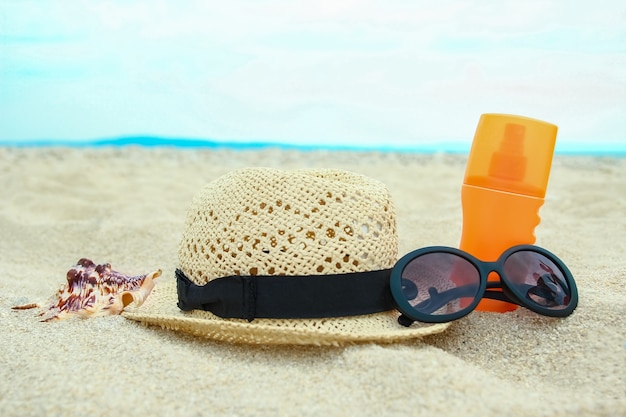 Hermoso sombrero con gafas y crema en el mar en la arena