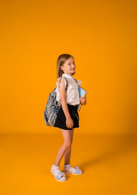 Hermoso uniforme de colegiala y con mochila destaca sobre un fondo amarillo con una copia del espacio. En pleno crecimiento