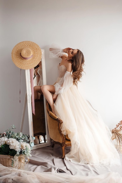 Hermoso vestido Longitud completa de una joven atractiva con un vestido de novia parada en el sillón cerca del espejo en una tienda de novias Foto de stock