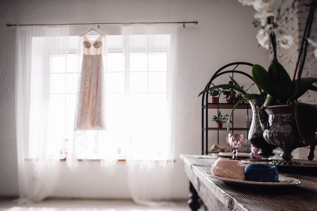 Hermoso vestido de novia colgado en la ventana durante la mañana de la novia