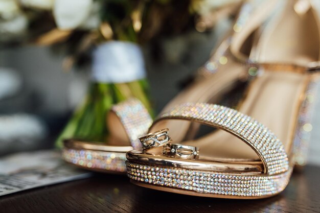 Hermosos anillos de boda dorados en una mesa de madera junto a un ramo y zapatos