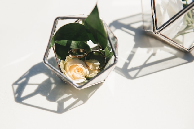 Hermosos anillos de boda con flores frescas en un recipiente de vidrio en el registro de matrimonio en el lugar