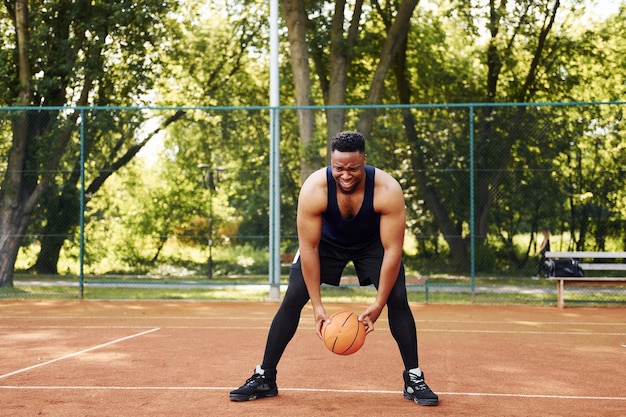 Hermosos árboles verdes en el fondo Hombre afroamericano juega baloncesto en la cancha al aire libre