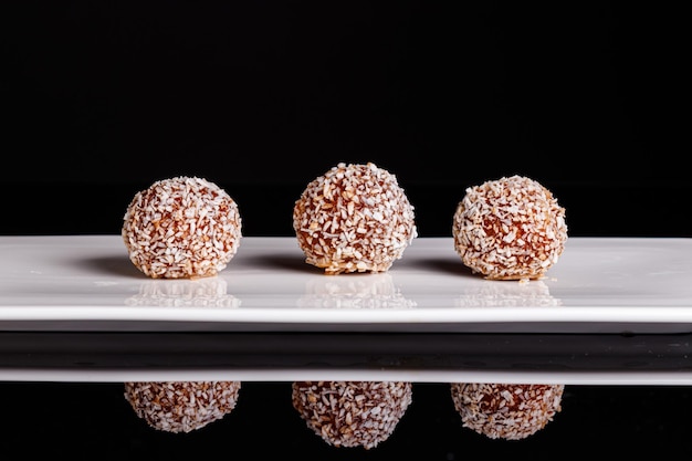 Hermosos dulces con coco en un plato blanco sobre un fondo negro