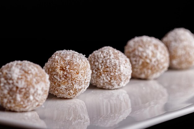 Hermosos dulces con coco en un plato blanco sobre un fondo negro