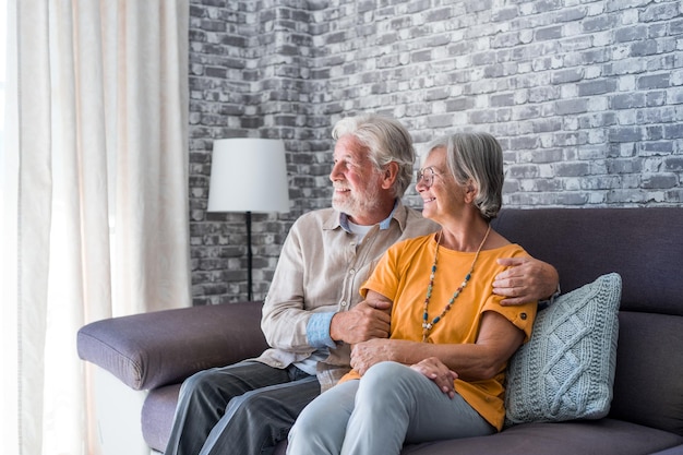 Hermosos esposos maduros de buen aspecto relajándose juntos en un cómodo sofá en una casa moderna sonriendo