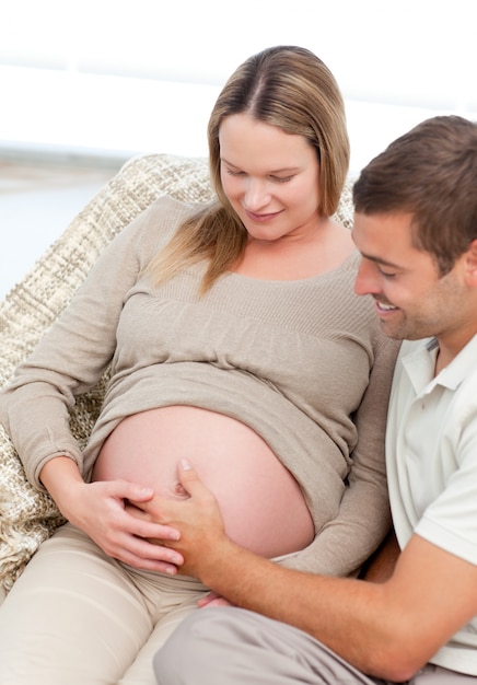 Foto hermosos futuros padres sintiendo a su niño por nacer sentado en el sofá