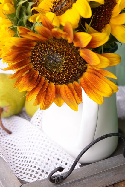 Hermosos girasoles en jarra con peras en la mesa de cerca