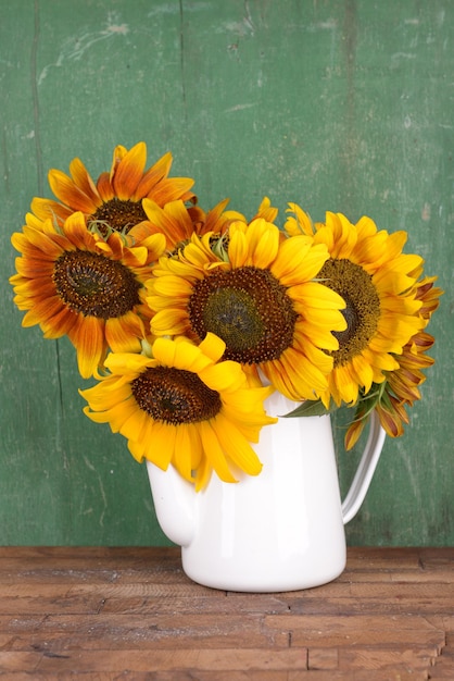 Hermosos girasoles en jarra sobre mesa sobre fondo de madera