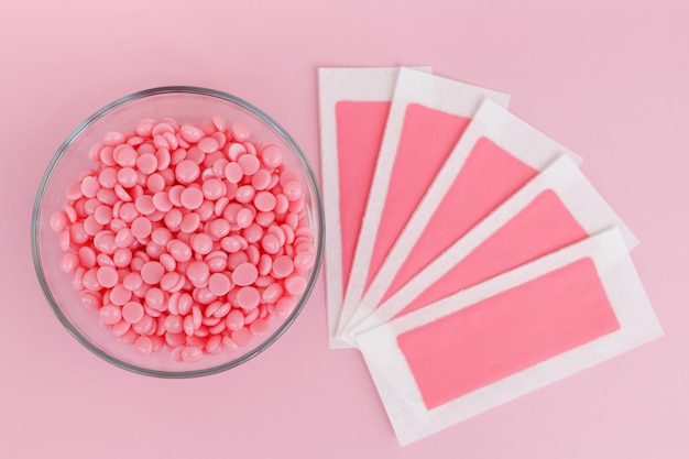 Hermosos gránulos de cera rosa y tiras depilatorias de cera para áreas delicadas sobre un fondo rosa