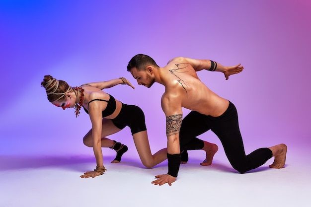 Hermosos jóvenes acróbatas o gimnastas con pintura facial colorida sobre fondo degradado azul rosa Pareja de ballet profesional bailando Dúo emocional interpretando arte coreográfico Instinto animal