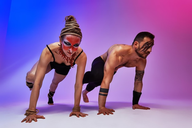 Hermosos jóvenes acróbatas o gimnastas con pintura facial colorida sobre fondo degradado azul rosa Pareja de ballet profesional bailando Dúo emocional interpretando arte coreográfico Instinto animal