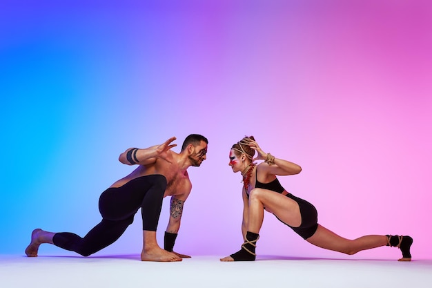 Hermosos jóvenes acróbatas o gimnastas con pintura facial colorida sobre fondo degradado azul rosa Pareja de ballet profesional bailando Dúo emocional interpretando arte coreográfico Instinto animal