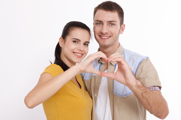 Hermosos jóvenes amantes se unen y sonríen, haciendo un marco de corazón con sus manos.