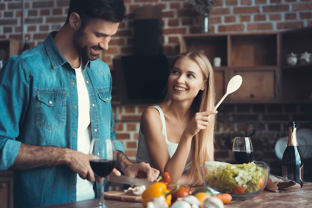 Hermosos jóvenes están hablando y sonriendo mientras cocinan alimentos saludables en la cocina de casa