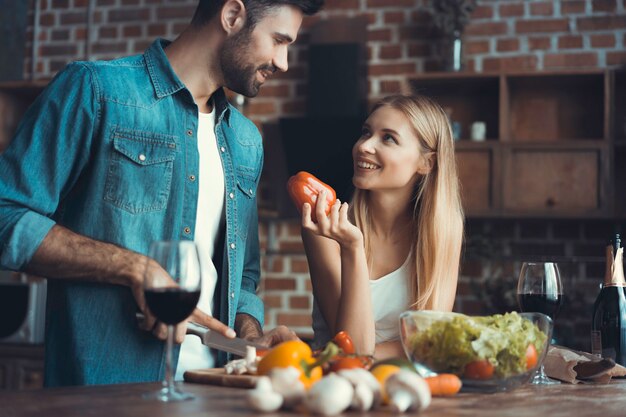 Hermosos jóvenes están hablando y sonriendo mientras cocinan alimentos saludables en la cocina de casa