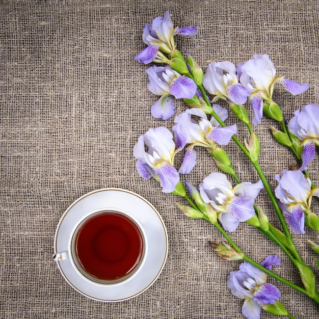 Foto hermosos lirios de flores púrpuras y una taza de té en una vista superior de fondo de lona gris