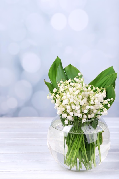 Hermosos lirios del valle en florero de vidrio sobre mesa de madera