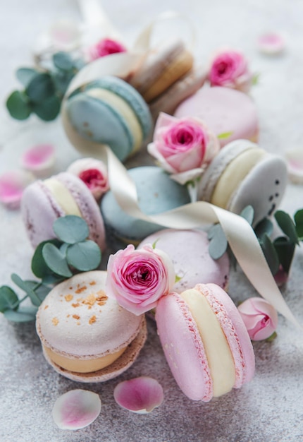 Hermosos macarrones sabrosos coloridos y rosas rosadas sobre un fondo de hormigón