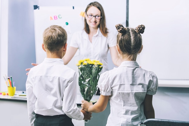 Hermosos niños escolares con flores para los maestros en la escuela en unas vacaciones