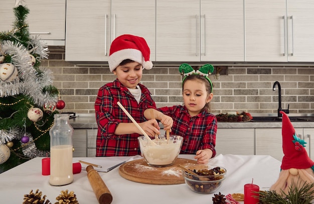 Hermosos niños europeos, hermosa niña en edad preescolar y guapo colegial, amoroso hermano y hermana preparando masa de pastel de Navidad juntos en la cocina de casa. Concepto de relaciones felices