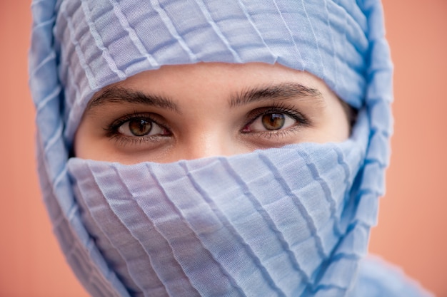 Hermosos ojos de joven musulmana con su rostro escondido detrás del hijab azul mirándote