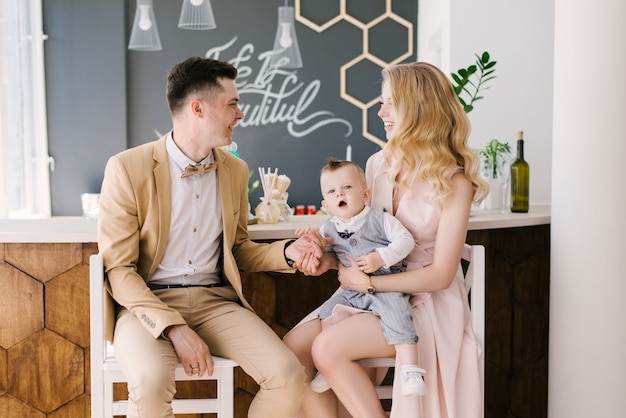 Hermosos padres jóvenes sonríen con su hijo de un año en casa en un hermoso interior en colores pastel. Aspecto familiar. Feliz cumpleaños fiesta