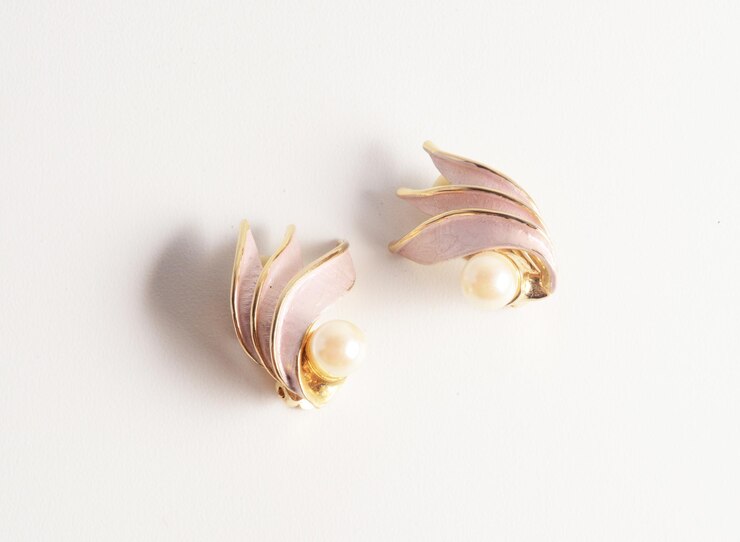 Hermosos pendientes de esmalte de satén rosa suave con perlas y bordes dorados sobre fondo blanco