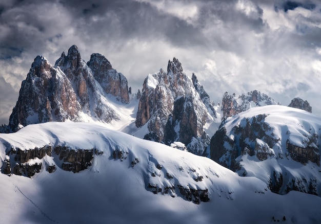 Hermosos picos de montaña en la nieve en invierno Paisaje dramático con altas rocas nevadas cielo nublado con nubes en la noche fría Tre Cime en Dolomitas Italia Montañas alpinas Naturaleza Paisaje oscuro