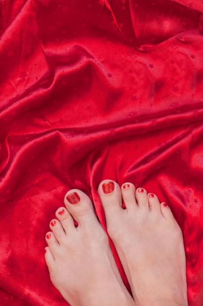 Hermosos pies femeninos con uñas de pedicura rojas sobre fondo textil de seda roja