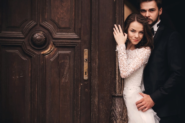 Hermosos recién casados abrazándose cerca de la puerta antigua