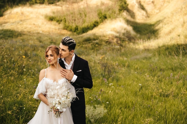 Hermosos recién casados abrazándose en la naturaleza Elegante pareja juntos en el fondo de las colinas