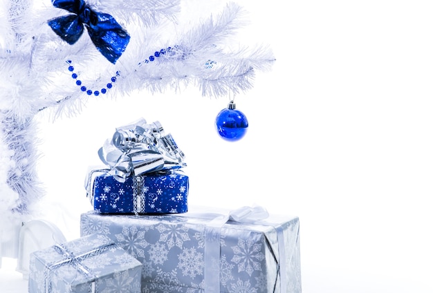 Hermosos regalos de Año Nuevo en color azul plateado parados debajo del árbol de Navidad sobre un fondo blanco.