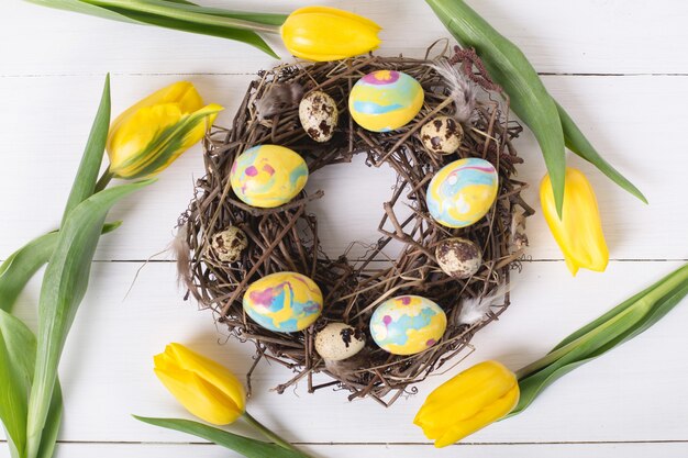 Hermosos tulipanes amarillos con codornices de colores y huevos de gallina en guirnalda en la mesa de madera blanca. Concepto de vacaciones de primavera y Pascua.