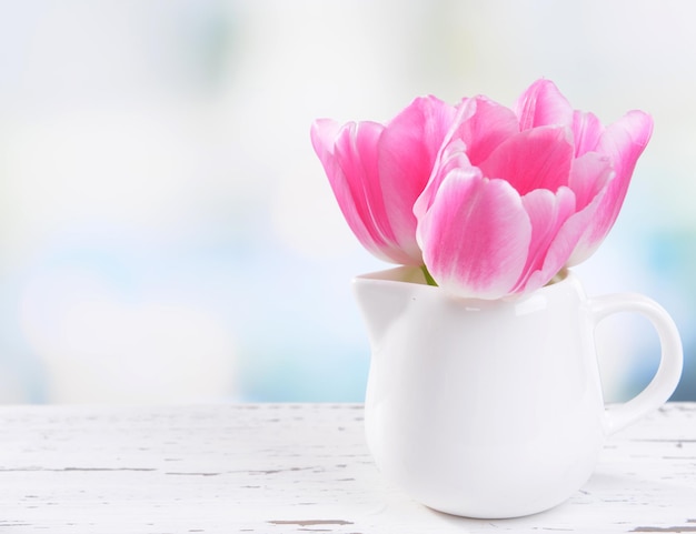 Hermosos tulipanes en balde en jarrón sobre mesa sobre fondo claro