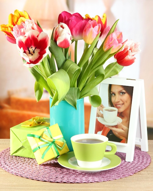 Hermosos tulipanes en balde con regalos y taza de té en la mesa en la habitación