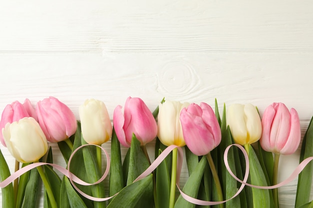 Hermosos tulipanes con cinta sobre fondo blanco de madera