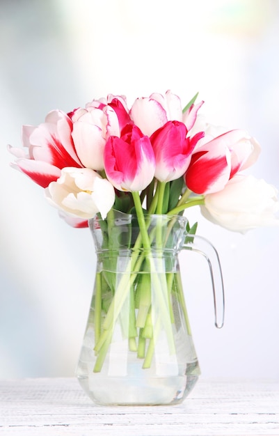 Hermosos tulipanes en jarra de vidrio sobre fondo claro