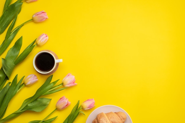 Hermosos tulipanes rosados, café y croissants sobre un fondo amarillo