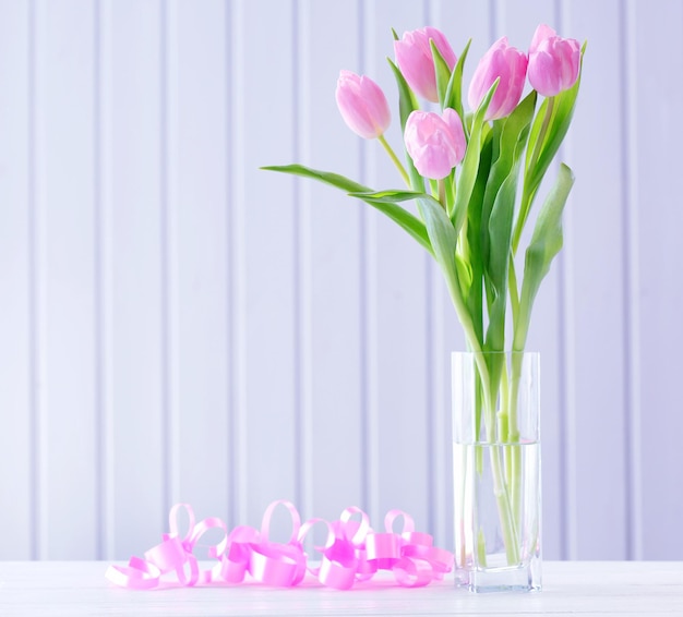 Hermosos tulipanes rosas en jarrón con corazones decorativos sobre fondo de madera