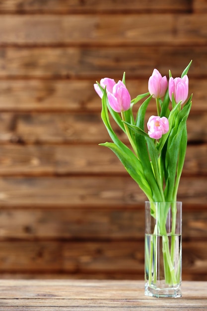 Hermosos tulipanes rosas en un jarrón sobre la mesa sobre fondo de madera