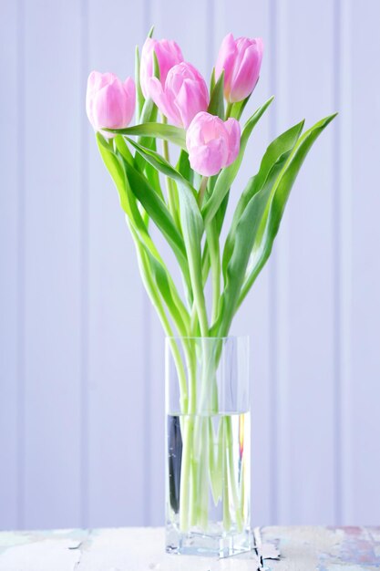 Hermosos tulipanes rosas en un jarrón sobre la mesa sobre fondo de madera