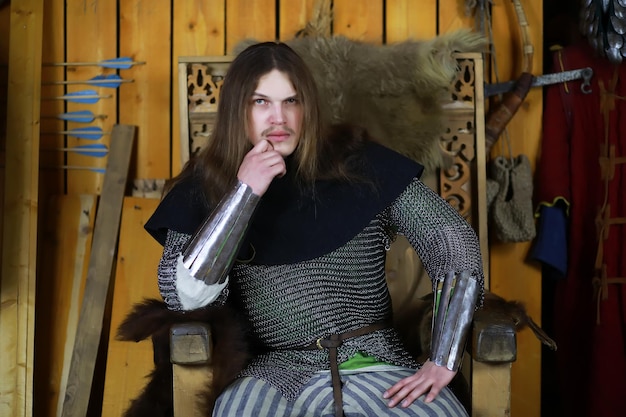 Un héroe poderoso con cabello largo y armadura de cota de malla en un salón antiguo. Guerrero medieval en las cámaras del caballero.