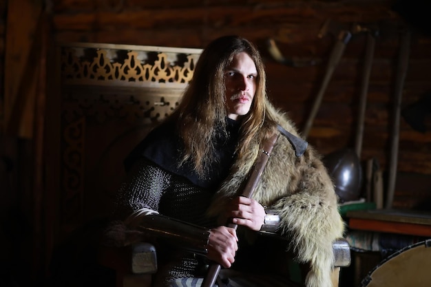 Un héroe poderoso con el pelo largo en una armadura de cota de malla en un antiguo salón. Guerrero medieval en los aposentos del caballero.
