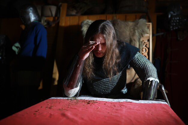 Un héroe poderoso con el pelo largo en una armadura de cota de malla en un antiguo salón. Guerrero medieval en los aposentos del caballero.